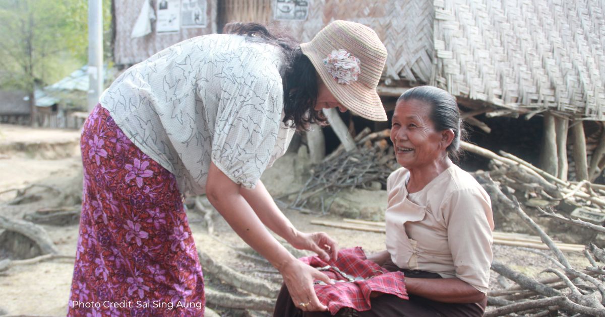 Dr Farhana Hoque bends to look at a coin garland in the lap of an older Marma woman, who is smiling as she shows the precious object.