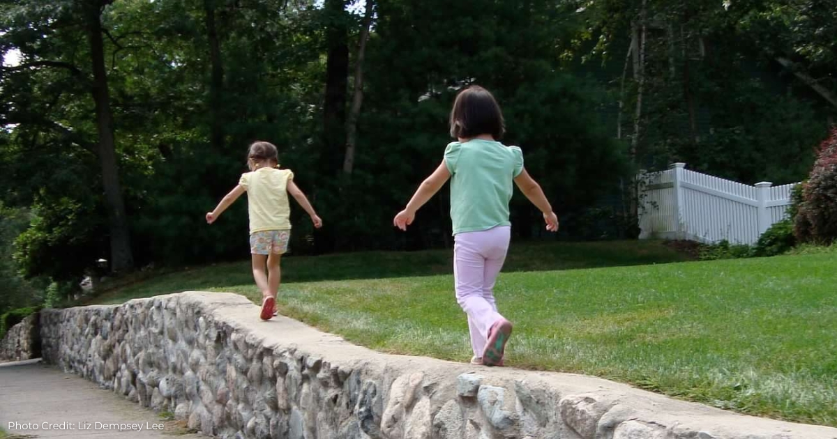 Two young kids playing; walking along a short stone wall.