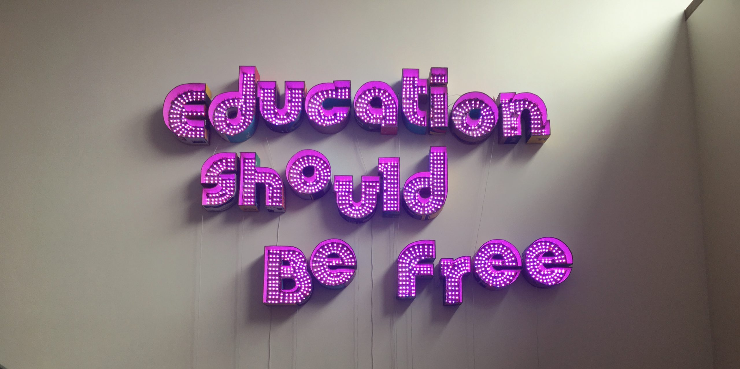 Purple neon letters on a wall that spell out "Education Should Be Free."