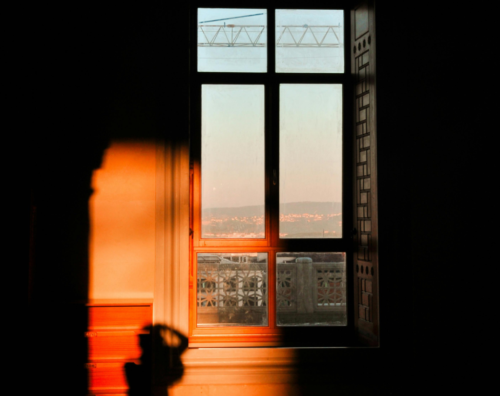 Shadow below a window overseeing a city landscape with an industrial crane in the background 